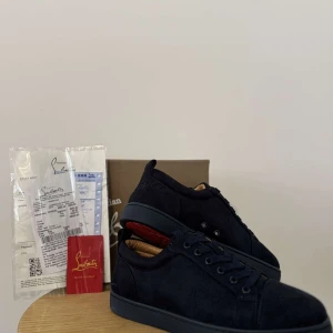 Mörkblå sneakers från Christian Louboutin - Snygga mörkblå sneakers från Christian Louboutin i mocka med klassisk röd sula. Skorna har rund tå, platt sula och snörning. Insidan är fodrad i beige skinn och detaljerna är stilrena och minimalistiska. Perfekta för dig som vill ha en exklusiv touch på din outfit.