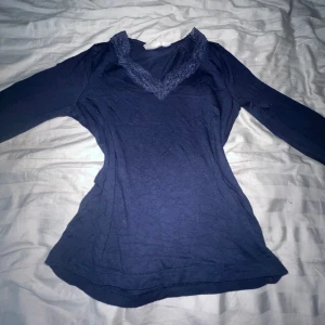 Mörkblå långärmad topp med spets - Supersnygg mörkblå långärmad topp från Gina Tricot med v-ringning och spetsdetaljer runt halsen. Säljer pga att jag fick denna i present men den är inte riktigt min stil, lappen sitter inte kvar.