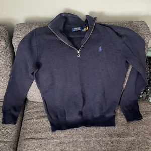 Marinblå half zip tröja Polo Ralph Lauren - Snygg marinblå långärmad tröja från Polo Ralph Lauren med half zip-dragkedja och klassisk broderad logga på bröstet. Tröjan har ribbade muddar och hög krage, perfekt för lager-på-lager-stil.