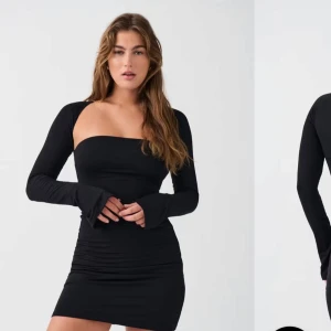 Svart långärmad kortklänning-Gina  - Supersnygg svart kortklänning med långa ärmar och figurnära passform. Klänningen har en rak, axelbandslös överdel och är tillverkad i ett stretchigt material som sitter tight. Perfekt för dig som gillar en stilren och trendig look.