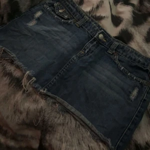 Jeanskjol  - Snygg blå jeanskjol med fransig kant och slitna detaljer. Klassisk femficksmodell med coola bakfickor och knäppning fram. Perfekt för dig som gillar en avslappnad och trendig stil. Säljer pågrund av att den va för stor