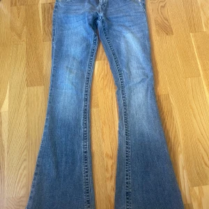 True Religion bootcut jeans blå - Snygga blå bootcut jeans från True Religion med klassiska kontrastsömmar och detaljerade bakfickor. Jeansen har låg midja och är tillverkade i slitstarkt denim med silverfärgade nitar och knappar. Perfekta för dig som gillar en retro vibe. Pris kan diskuteras!