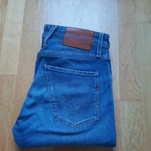 Blå Replay anbass jeans  - Säljer ett par klassiska blå jeans från Replay i ekologisk bomull. Modellen är anbass, fem fickor och snygga detaljer på bakfickorna. Sköna och stilrena jeans som passar till det mesta. Midjan är normal och passformen är straight. Storleken på byxorna är 29/34