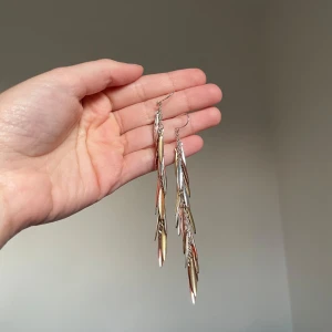 Långa metallic örhängen i guld och silver - Säljer ett par riktigt snygga långa örhängen med flera smala, avlånga hängen i både guld- och silverfärg. De har en cool, kedje-liknande design som ger ett statement-utseende och passar perfekt om du vill sticka ut. Örhängena är lätta och rör sig snyggt när du bär dem.