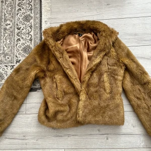 Brun pälsjacka med satinlining - Säljer en snygg brun pälsjacka från H&M med mjukt foder i satin. Jackan har klassisk krage, långa ärmar och en schysst croppad passform. Perfekt för dig som vill sticka ut med en trendig look i höst och vinter.