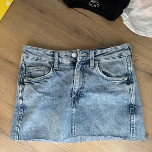 Ljusblå jeanskjol med rå kant - Säljer en ljusblå jeanskjol i kort modell med klassiska fickor fram och bak. Kjolen har en rå, fransig kant nertill och bälteshällor i midjan. Perfekt för dig som gillar en avslappnad och trendig stil. För liten på mig i midjan som brukar ha 38/m 