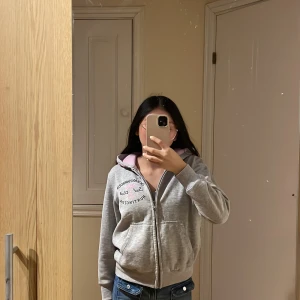 Grå hoodie  - Säljer en grå hoodie från Ocean Harbour med dragkedja och en rosa insida av huvan. Perfekt för en avslappnad stil. Den har långa ärmar och en tryckt logga på bröstet. Skön och praktisk för vardagsbruk.