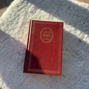 Little Women av Louisa May Alcott - Säljer en vacker röd inbunden utgåva av 'Little Women' av Louisa May Alcott. Boken har gulddetaljer på omslaget och innehåller bilder från filmatiseringen. Perfekt för samlare eller som en fin present!