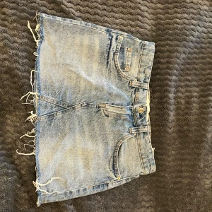 Blå jeanskjol - Snygg blå jeanskjol med rå kant och klassisk femficksdesign. Perfekt för en avslappnad stil. Kjolen har en knapp och dragkedja framtill.