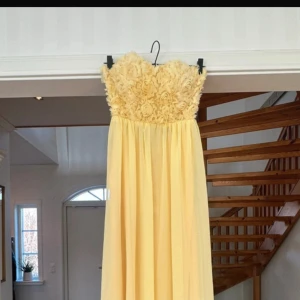 Gul axelbandslös klänning med blommig detalj - Fin balklänning som jag köpte second hand med som inte passade. Tidigare användare hade endast använt den ett fåtal gånger men ser helt ny ut💕