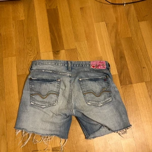 Jeansshorts med fransar - Snygga jeansshorts i ljusblå denim med fransiga kanter. De har en klassisk femficksdesign och en rosa etikett bak. Från replay. Passar inte mig längre så sitter tight, man hade kunnat dra upp de också beroende på hur korta man vill ha de men det kan inte jag göra tyvärr. Midjemått tvärsöver 39cm