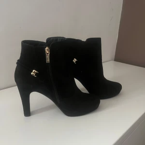 Svarta stövletter med dragkedja från Tamaris - Snygga svarta stövletter i mocka med guldfärgade dragkedjor och detaljer. Oanvända. Hund finns i hemmet