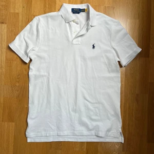 Vit pikétröja från Ralph Lauren - Säljer en klassisk vit pikétröja från Ralph Lauren med loggan broderad i blått. 10/10 skick och har aldrig använts. säljer pga. råkade köpa för stor storlek. Perfekt för en avslappnad och stilren look till sommaren🙌✅bara att kontakta vid ytterligare frågor!