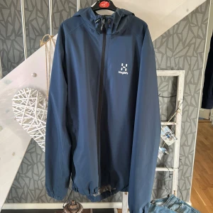 Blå vindjacka från Haglöfs - Säljer en blå vindjacka från Haglöfs med dragkedja och huva. Jackan har en stilren design med Haglöfs logotyp på bröstet. Perfekt för blåsiga dagar och utomhusaktiviteter. Jackan är i mycket bra skick, hörr av dig om du undrar något // William 