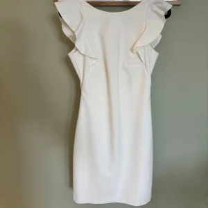 Oanvänd studentklänning  - Vit klänning med volangdetaljer vid axlarna och en djup v-ringad rygg. 