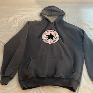 Grå hoodie från Converse - Säljer en grå hoodie från Converse med det klassiska All Star-märket på bröstet. Tröjan har en stor ficka framtill och en justerbar huva. Det var min pappas innan han gick bort så därför är storleken stor