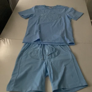Ljusblå shorts och t shirt  från Risky - Snygga ljusblå shorts och t shirt  från Risky med en cool logga på framsidan. De har en bekväm passform, Perfekta för en avslappnad stil. Använd 2-3 gånger köpt för 1000kr