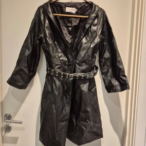 Svart skinnklänning från NA-KD - Snygg svart skinnklänning från NA-KD, Hannalicious kollektion. Klänningrn har trekvartsärmar och ett coolt bälte i midjan. Fint skick, något skrynkliga bara då den flyttats med till nytt boende.