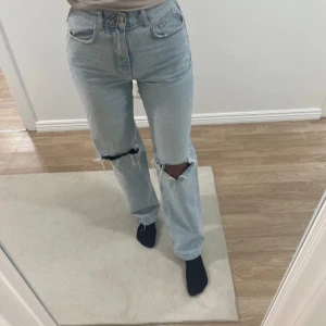 Ljusblå jeans med slitningar - Snygga ljusblå jeans och slitningar på knäna. De har en klassisk femficksdesign och en knappgylf. Perfekta för en avslappnad stil. Från Gina tricot!