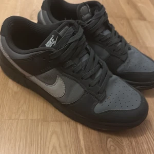 Svarta och grå Nike sneakers - Säljer ett par stilrena Nike sneakers i svart och grått. Skorna har en klassisk design med snörning och perforerade detaljer på tån för extra ventilation. Perfekta för både vardag och träning.