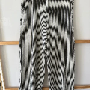 Randiga byxor från MaxMara - Snygga randiga byxor från MaxMara i svart och vit. Byxorna har en klassisk design med knappar och bälteshällor. Perfekta för en stilren look.