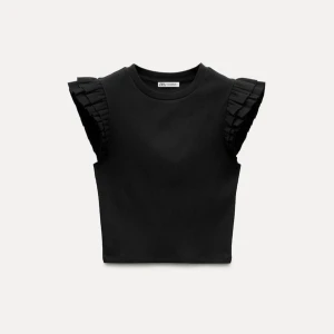 Svart topp med volangärmar från Zara - Snygg svart topp från Zara med volangdetaljer på ärmarna. Toppen är ärmlös och har en croppad passform som ger en trendig look. Perfekt för att styla med jeans eller kjol. 