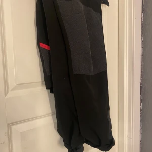 Svarta byxor från High Mountain - Säljer ett par svarta byxor från High Mountain med gråa detaljer och rosa dragkedjor. Byxorna har flera praktiska fickor och är perfekta för utomhusaktiviteter. De är designade för att vara både funktionella och stiliga.