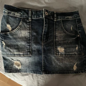 Jeanskjol från ONLY - Snygg jeanskjol från ONLY med slitna detaljer och femficksdesign. Kjolen har en klassisk blå denimfärg och är perfekt för en avslappnad stil. Den har bälteshällor och stängs med knapp och dragkedja framtill. Kjolen är köpt i Grekland och är en gammal modell från only, är köpt på 125 kr och är använd endast en gång. Skriv om ni vill ha bild på hur den sitter på och använd helst inte köp knappen❤️