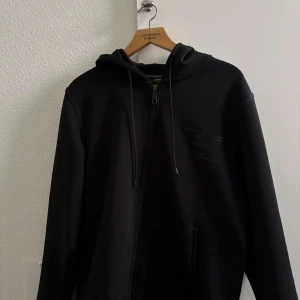 Svart hoodie från Boss - Snygg svart hoodie från Boss med dragkedja och justerbar huva. Perfekt för en avslappnad stil. Rkt snygg, köpt från Urban Modern för någon månad sedan.