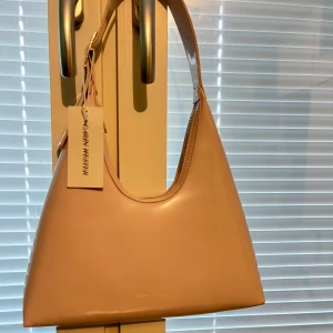 Ljusrosa axelväska från Ahlens - Snygg ljusrosa axelväska från Åhlens med stilren design. Väskan har en justerbar axelrem med spänne och en minimalistisk look. Perfekt för att bära dina dagliga nödvändigheter med stil.