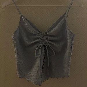 Urringad topp - En urringad/öppen topp fram från H&M i storlek S. Den är ljusblå glittrig med knyte fram. Har även en volang under knytet. Aldrig använd. Ny med prislapp.