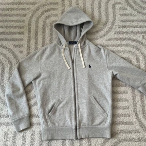 Grå zip hoodie från Ralph Lauren - En grå hoodie från Ralph Lauren. Den är använd ytterst lite o är därav i nyskick. Med justerbar huva och den ikoniska loggan broderad på bröstet. Den är i strl S och passar mig perfekt som är ca 174👌Kontakta vid fler frågor👍