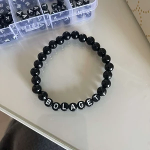 Svart pärlarmband med text - Snyggt svart pärlarmband med bokstäver som bildar ordet 'BOLAGET'. Perfekt accessoar för en personlig touch. Elastiskt band för enkel passform.