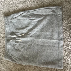 Grå sweatkjol från GANT - Grå mjuka sweatkjol från GANT med klassisk logga broderad framtill. Kjolen har snörning i midjan och två sidofickor. Perfekta för chill, tillverkade i bomullsmix för skön känsla. Enkel och stilren design som funkar till allt.