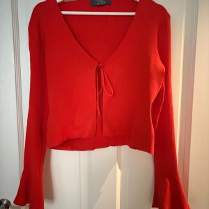 Röd croppad ribbad topp Primark - Snygg röd croppad topp från Primark med långärmade trumpetärmar och djup v-ringning. Ribbad struktur och knyt framtill.