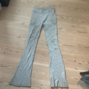 Grå ribbade bootcut mjukis byxor - Säljer ett par grå ribbade byxor med bootcut och hög midja. De är stickade och har en mjuk, stretchig känsla som gör dem riktigt sköna att bära. Perfekta för dig som gillar en chill och trendig look med lite extra flair i benen. Byxorna är väldigt stretchiga