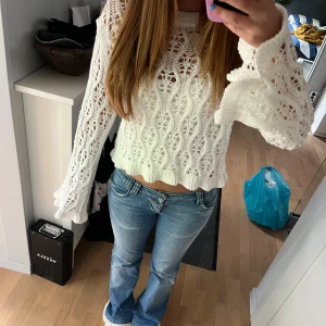 Vit stickad tröja - Säljer en vit stickad tröja från H&M Divided i storlek S. Tröjan är croppad med långärmade ärmar och har ett snyggt hålmönster och vågiga kanter vid ärmslut och nederkant. 