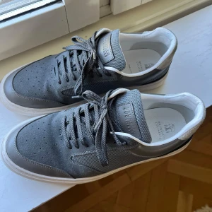 Brunello Cucinelli sneakers - Snygga grå sneakers från Brunello Cucinelli med vit sula och detaljer i mocka, mesh och skinn. Låg modell med rund tå och snörning. Perfekt för dig som gillar stilrena och exklusiva sneakers med coola materialmixar.