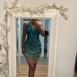 Glittrig blå kortklänning med paljetter Jovanni  - Säljer en superfin kort klänning från märket Jovanni nypris 6900 kr i turkos blå med glittriga paljetter med äkta swarowski stenar. Klänningen har v-ringad hals, ärmlös halterneck design med öppen rygg och inbyggda kupor för extra stöd. Perfekt för dig som vill sticka ut med en unik look! Strl XS 