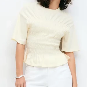 Ljusgul blus från Gina Tricot - Supersöt ljusgul blus med korta ärmar och rund hals från Gina Tricot. Toppen har smockad midja som ger en snygg form och avslutas med en liten volangkant nedtill. Aldrig använt! Nu utan prislapp ( storlek m som passar mig som har s perfekt) slutsåld på nätet 