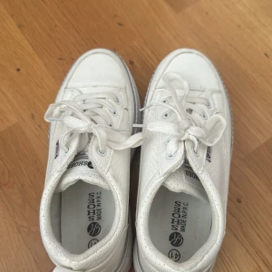 Vita sneakers från YS Shoes, strl 41 - Fräscha vita sneakers från YS Shoes med klassisk rund tå och platt sula. Skorna har perforerade sidor för extra ventilation och snygga vita snören. Perfekt för dig som gillar stilrena och sportiga skor med en clean look.