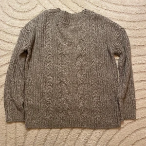 Brun stickad tröja från bpc - Säljer en gråbrunmelerad stickad tröja från bpc bonprix collection. Tröjan har ett snyggt flätmönster framtill, rund hals och långa ärmar. Perfekt för dig som gillar en chill och klassisk look. Materialet är mjukt och värmande. 