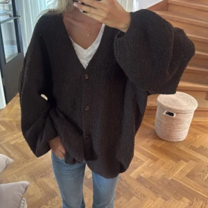 Oversized brun kofta med knappar - Mysig oversized kofta i mörkbrunt med v-ringning och tre knappar framtill. Materialet är fluffigt och stickat, perfekt för att slänga på sig över en t-shirt. Passar dig som gillar chill och avslappnad stil. s/m