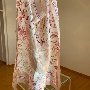 Beige och rosa blommig sjal - Snygg och tunn halsduk i siden med blommigt mönster i beige och rosa toner. Sjalen har en fyrkantig form och dekorativa rosa ränder längs kanten.