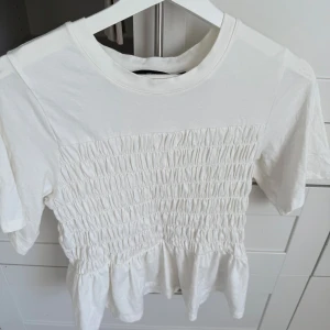 Vit blus med smock från Vero Moda - Supersöt vit blus från Vero Moda i storlek M. Toppen har korta ärmar och ett smockat parti över bröstet som ger en cool och trendig look. 
