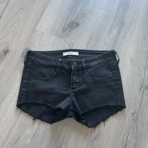 Lågmidjade shorts - Svarta jeansshorts från Hollister med låg midja och råa, fransiga kanter. Klassisk femficksmodell med knapp och dragkedja framtill. Snygg, enkel design som passar perfekt till sommaren. Materialet är mjukt och stretchigt denim för skön passform.