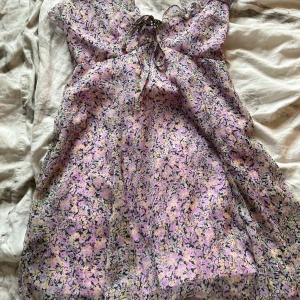 Ljuslila blommig klänning Gina Tricot - Supersöt kortklänning från Gina Tricot i storlek XS. Klänningen har ett blommigt mönster i lila, gul och svart, med volangdetaljer och knyt framtill vid halsen. Materialet är lätt och luftigt, perfekt för varma dagar. Passformen är normal och ärmarna är korta.