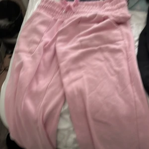 Rosa mjukisbyxor med snörning - Säljer ett par ljusrosa mjukisbyxor med elastisk midja och snörning framtill. Byxorna har två bakfickor och är tillverkade i mjukt bomullsmaterial. Perfekta för chill dagar eller när du vill vara extra comfy. Passformen är loose och färgen är riktigt söt.