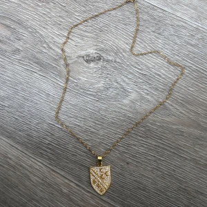 Guld halsband/ Sandzak halsband - Unikt halsband i guldton med tvinnad kedja och sandzak symbolen. Symbolen är täckt av gnistrande stenar och har detaljer som månar och liljor. Perfekt för dig som vill sticka ut med något riktigt speciellt.