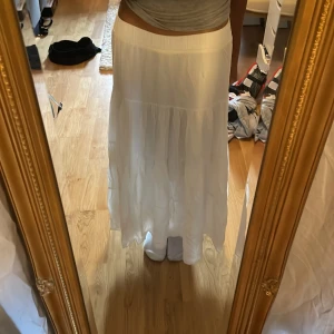 Vit långkjol i luftig bomull - Säljer en vit långkjol med volanger och elastisk midja. Den har dubbel lager och är inte genomskinlig. Kjolen är lite kort för mig som är 158cm. Kjolen är riktigt flowy och gjord i tunn, luftig bomull som passar perfekt till varma dagar. Enkel att styla med crop top eller linne för en chill vibe.